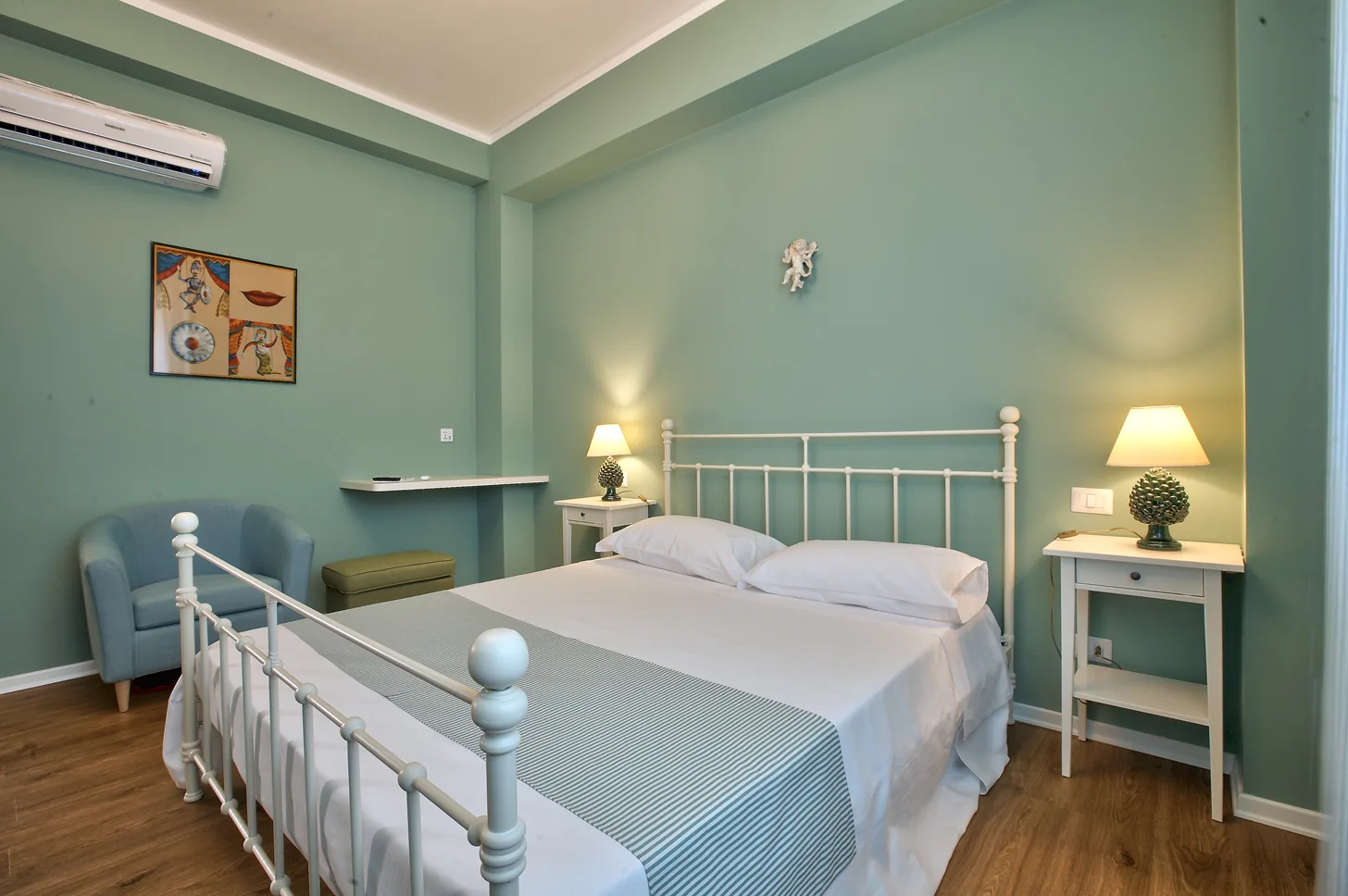 The second space of the Green Room: the white wrought-iron bed, the armchair and the painting of Sicilian masks