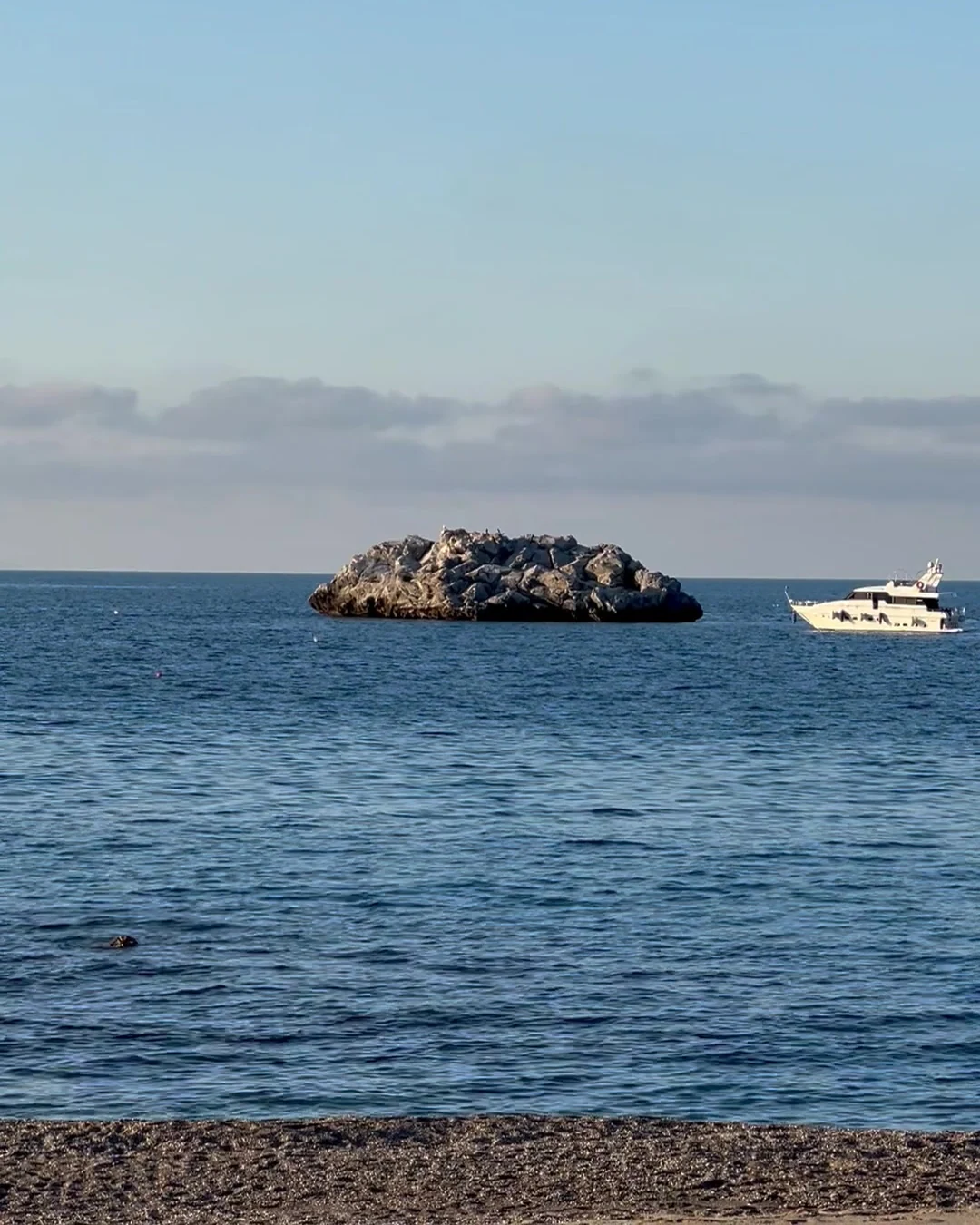 The beach at Brolo on a February day, with the rock offshore and a boat passing