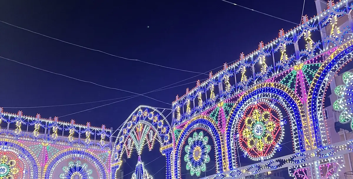 Luminarie a rosoni colorati sopra il centro durante la festa patronale