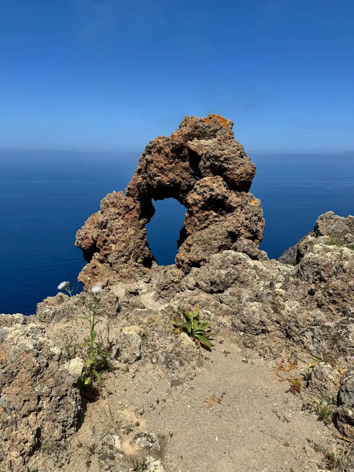 An arch of reddish volcanic rock on the ridge, with the open sea showing through the opening