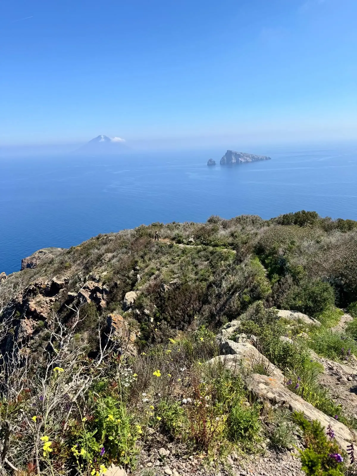 The ridge path with a walker on it, and Stromboli and Basiluzzo on the horizon