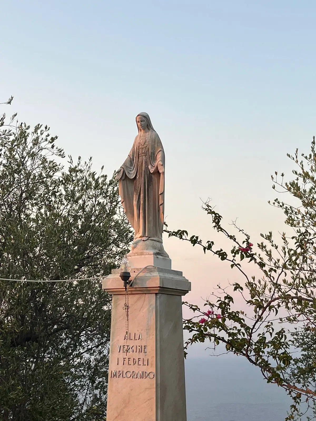 Statua della Vergine con l'iscrizione «Alla Vergine i fedeli implorando», sul mare al tramonto