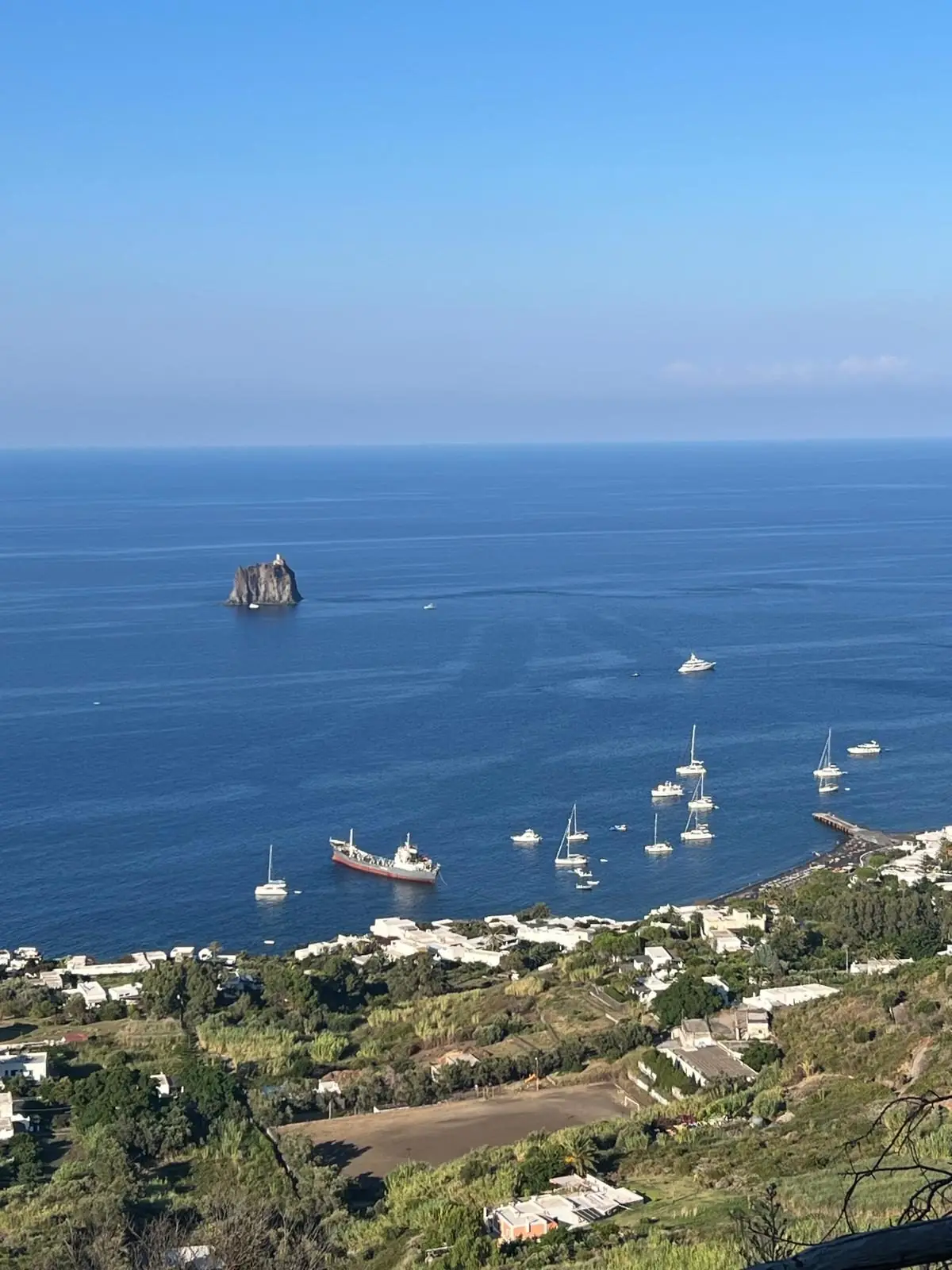 From high on the trail: the white houses of the village, boats at anchor and the rock of Strombolicchio out at sea