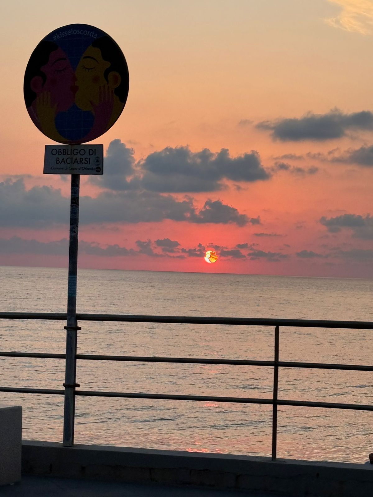 Il cartello «Obbligo di baciarsi» sul lungomare, al tramonto