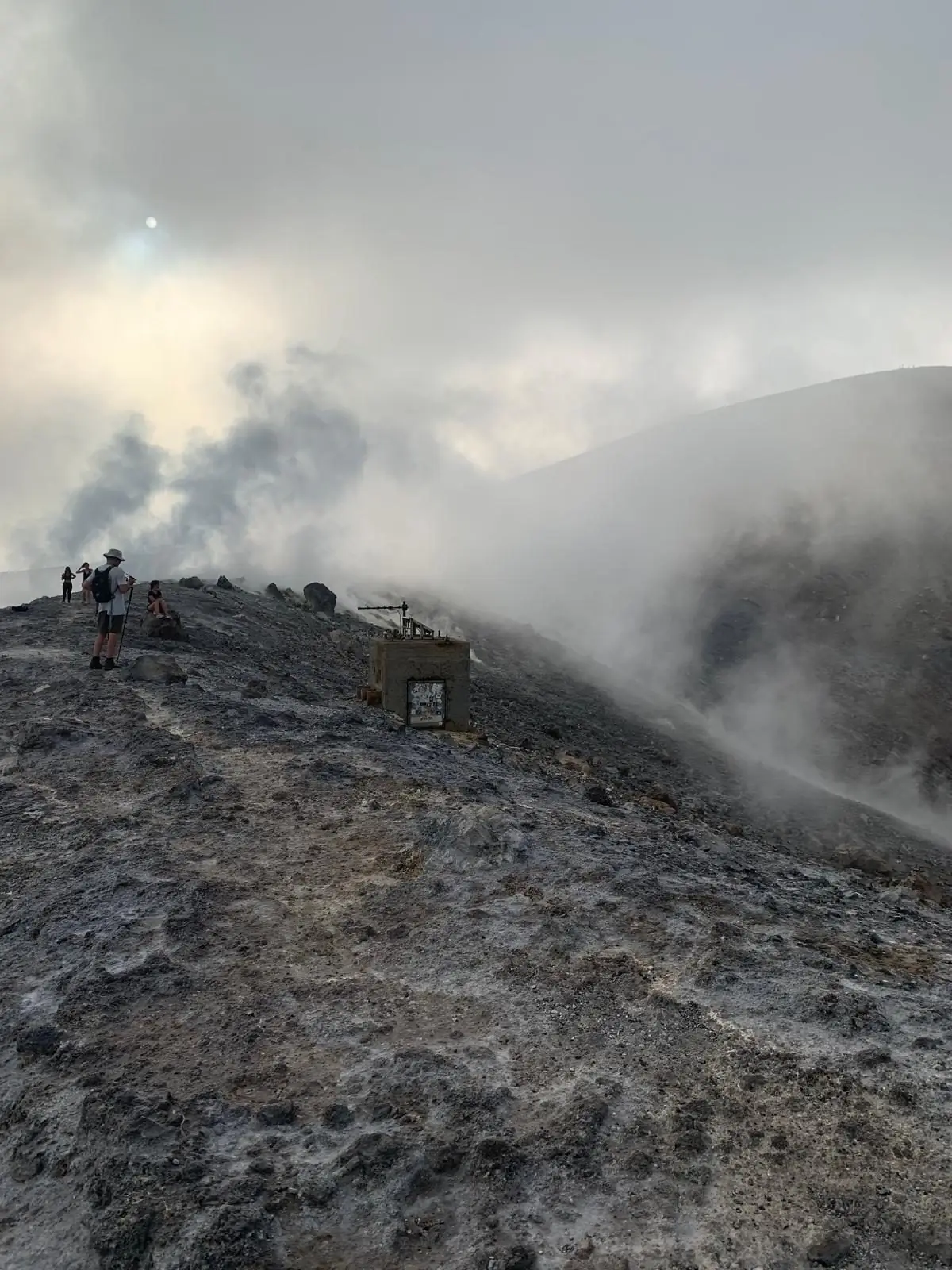 Fumaroles venting from the crater rim, wrapping walkers and the monitoring station in steam