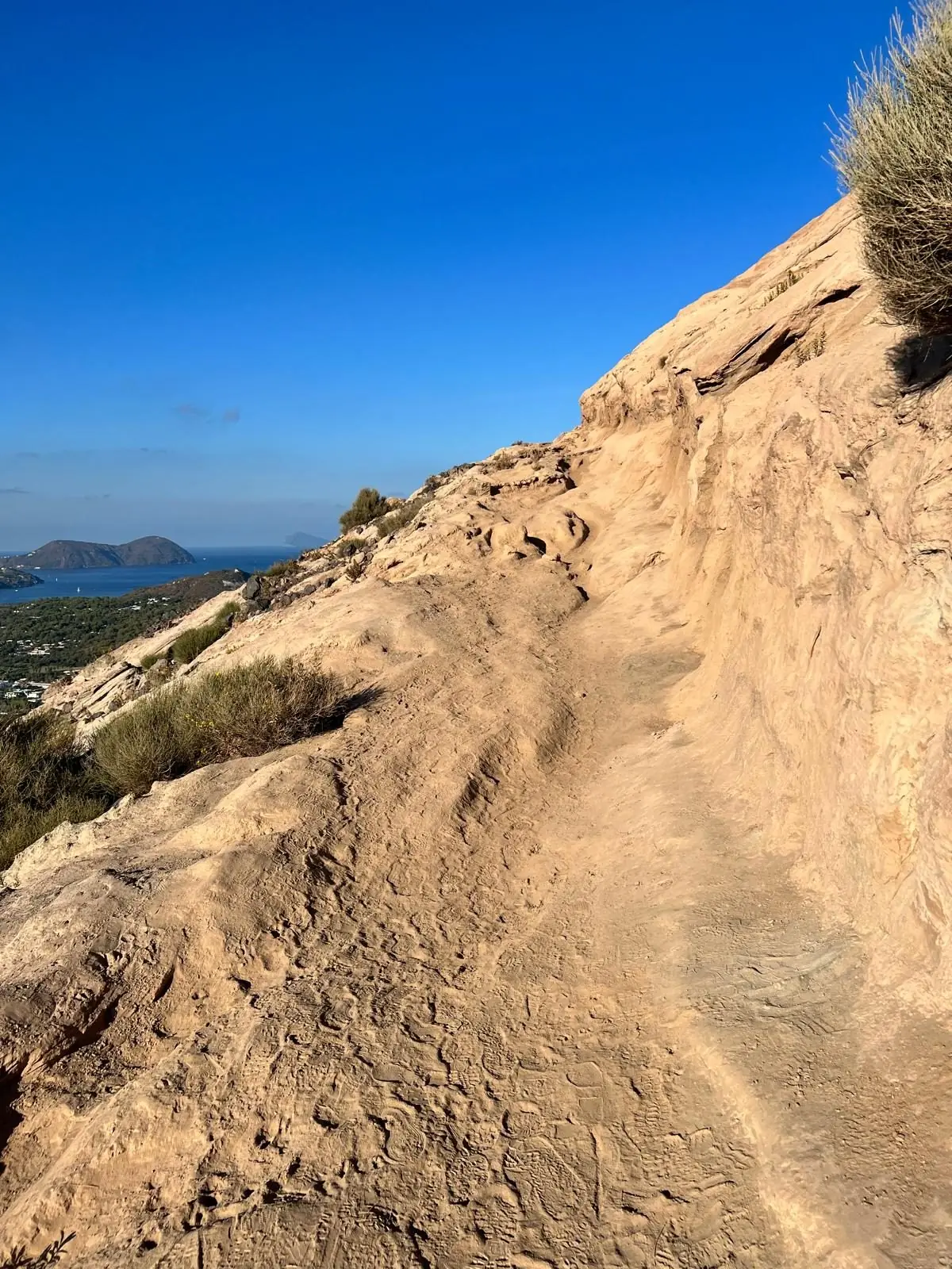 The path cut into pale tuff climbing towards the crater in early morning light, with the islands on the horizon